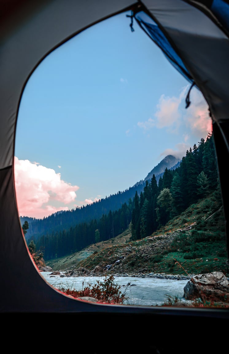 Camping tent on shore of rapid river in mountainous terrain